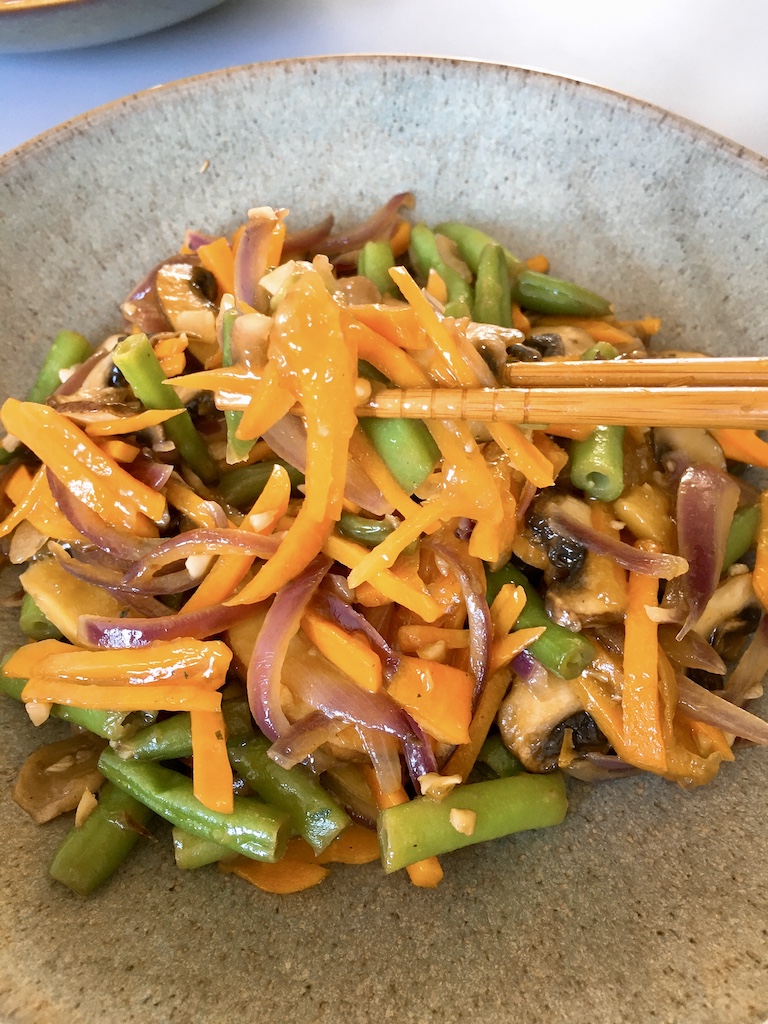 Picking up veggies stir-fry with chopsticks.