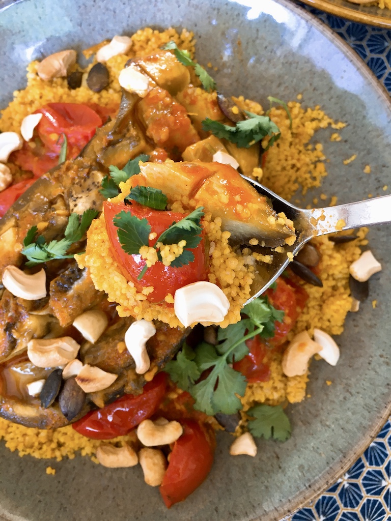 A spoon of aubergine curry with crunchy nuts, tomatoes and couscous.