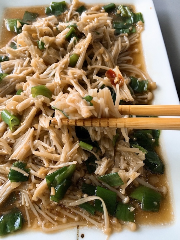 Picking up chopped enoki mushroom with chopsticks.