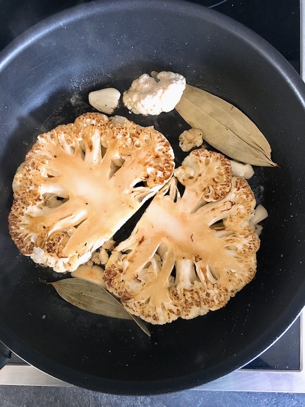 Pan-searing cauliflower steak with smashed garlic and bay leaves.