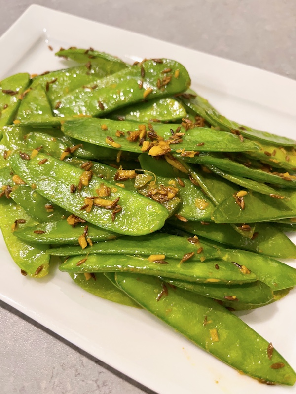 A plate of stir-fry mangetout with cumin and turmeric.