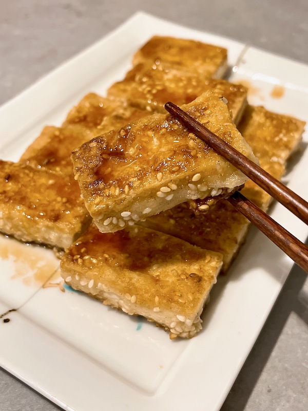 A piece of crispy tofu picking up by chopsticks.