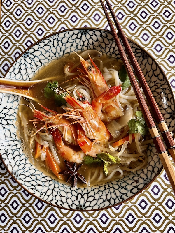 A bowl of prawn noodle soup with chopsticks.