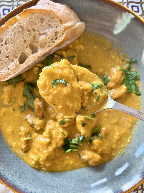 A spoon of cooked white fish in almond curry sauce.