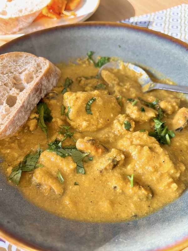 A bowl of almond curry sauce with seafood and baguette.