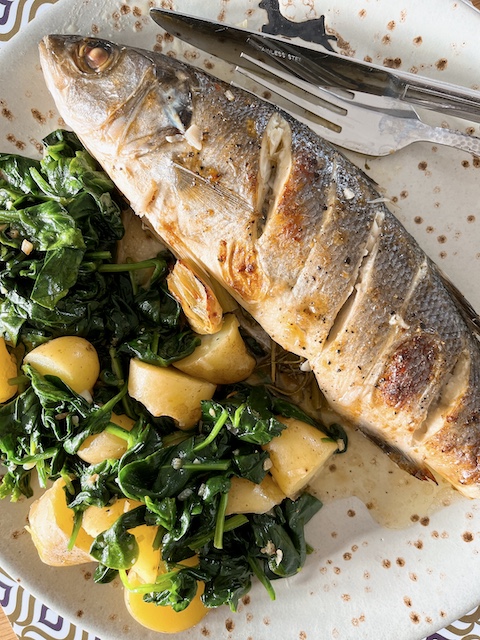 Baked whole sea bass with blitva-inspired spinach and potatoes.