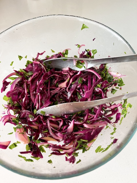 Picking red cabbage slaw with tongs.